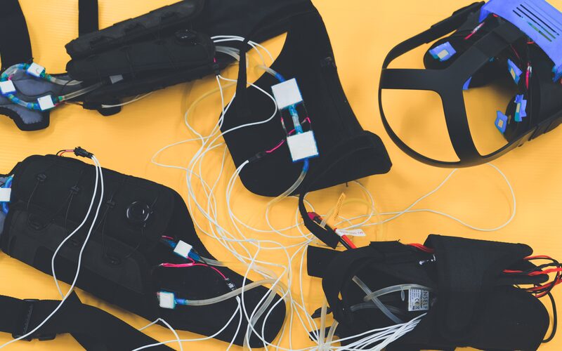 Wearable thermal feedback hardware laid out on a table: arm sleeves, neck module, controller and a VR headset with thermal modules